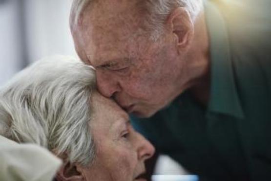 an elderly man kissing his wife's forehead 